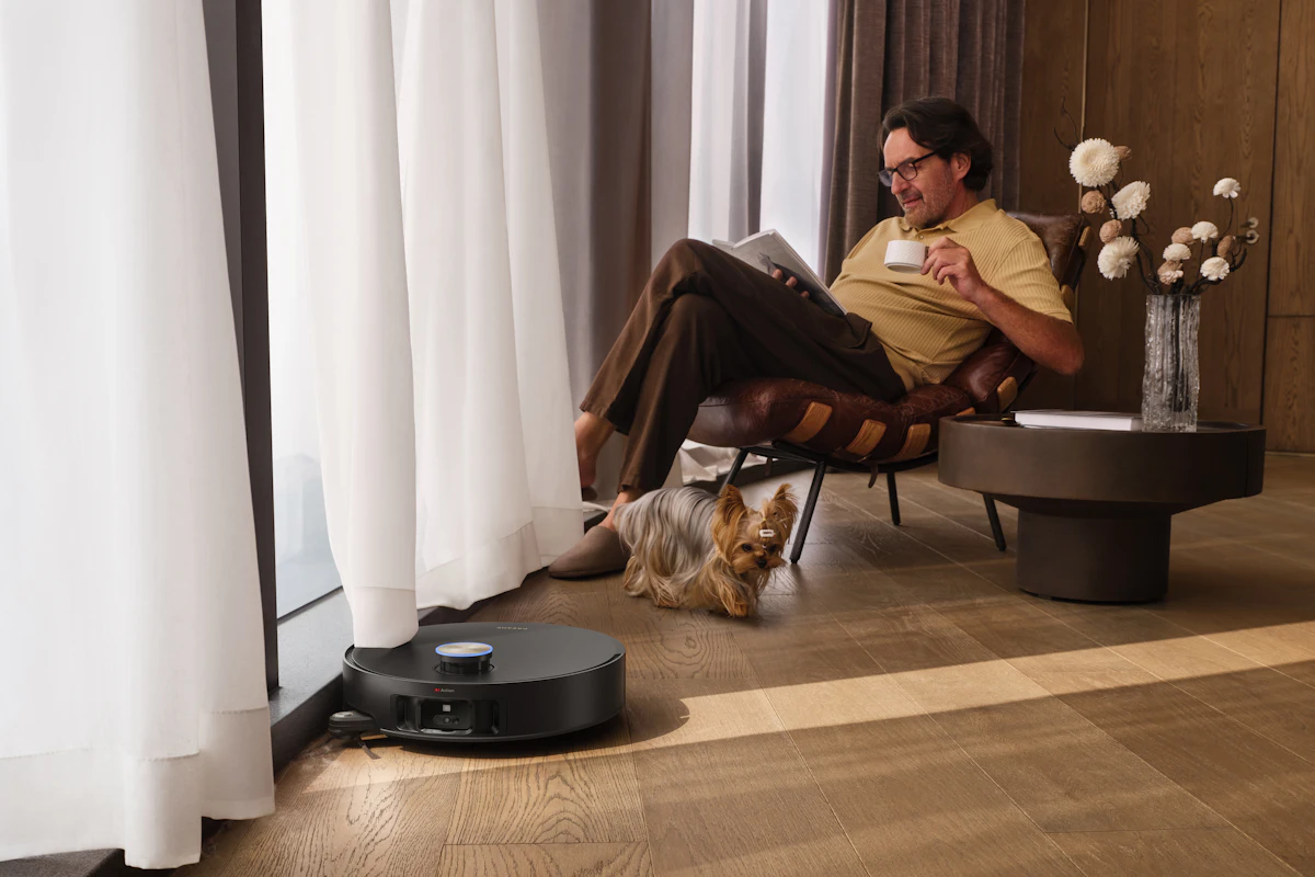 Homme qui se détend avec un café pendant qu'un aspirateur robot nettoie le sol